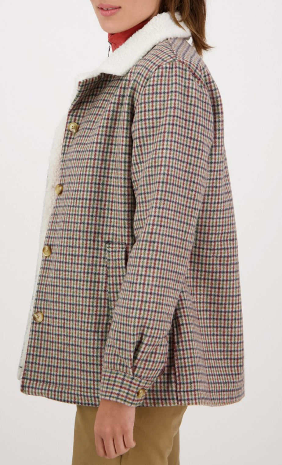 A person wearing a Swanndri Capitola Sherpa Jacket with a plaid pattern and white fleece collar, paired with tan pants, is shown from the side against a plain background with their face partially out of view.