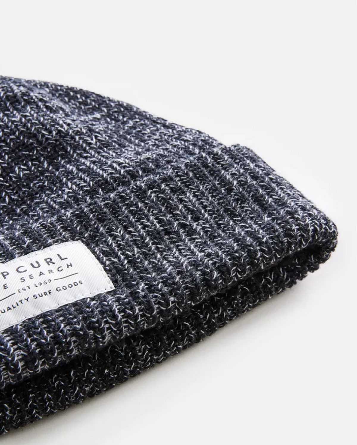 A close-up of the gray Rip Curl Dusk Fleece Lined Regular Beanie, neatly folded with a white fabric tag displaying small printed text, set against a plain white background.