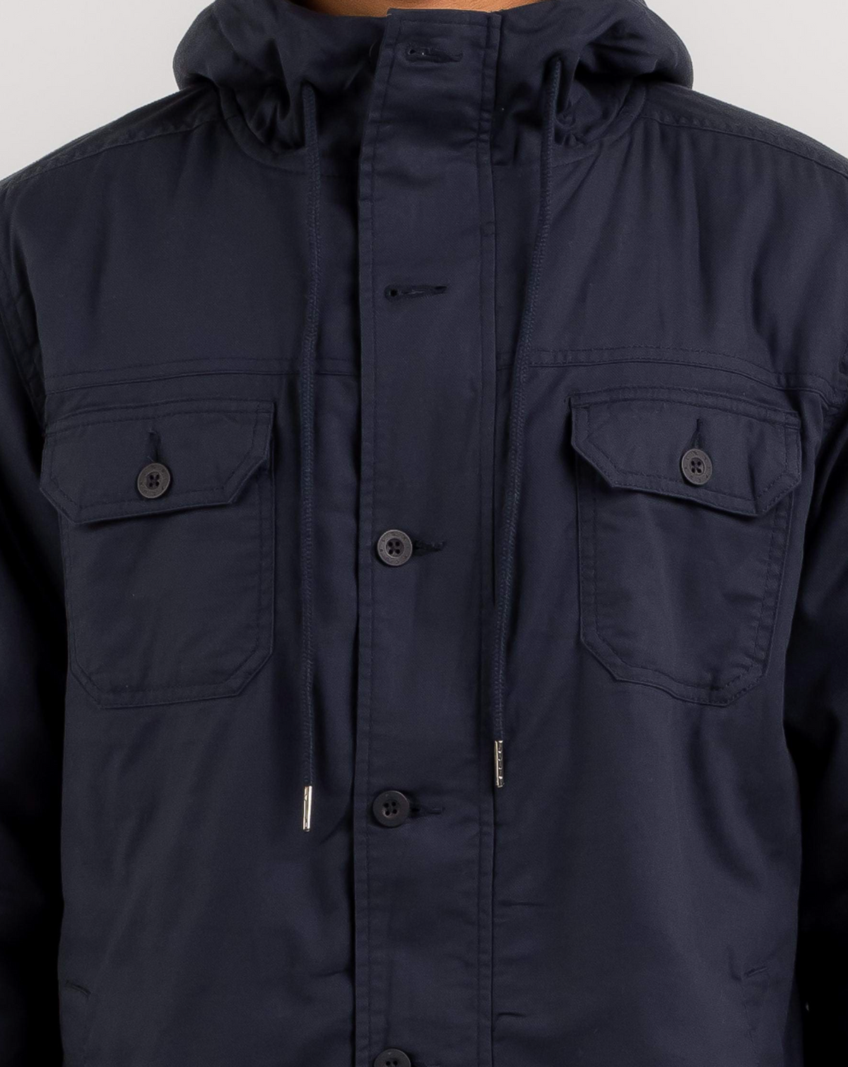 The person is wearing a Rip Curl Gibbos Jacket, featuring a navy blue button-up design with two chest pockets, drawstrings, and a high collar. The jacket blends style and functionality, though the person's face is not visible.