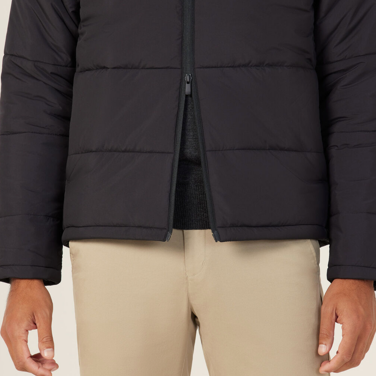 A person wears the NNT Puffer Jacket, a stylish black puffer with 3M Thinsulate, over a dark shirt and beige pants. Shown from shoulders to mid-thigh, their arms are relaxed at their sides.