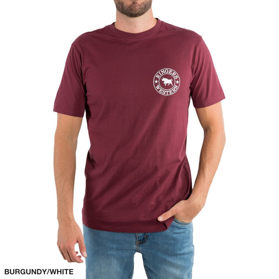Someone is wearing a burgundy Ringers Western Signature Bull Classic T-Shirt made of 100% cotton. It has a circular white horse logo on the left chest and is paired with blue jeans. The text in the corner reads "BURGUNDY/WHITE.