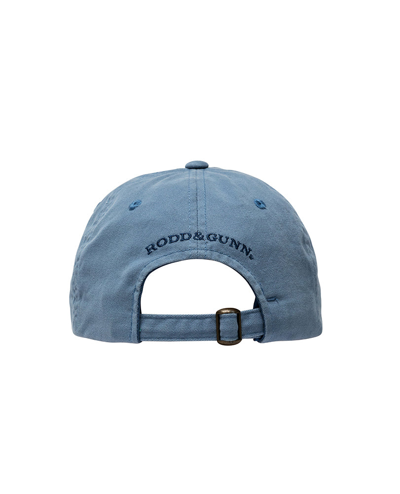 A Rodd & Gunn Signature Cap in blue, seen from the back, showcases the black embroidered Rodd & Gunn logo above its adjustable strap with a metal buckle. Made of cotton twill, this cap has a slightly worn texture.