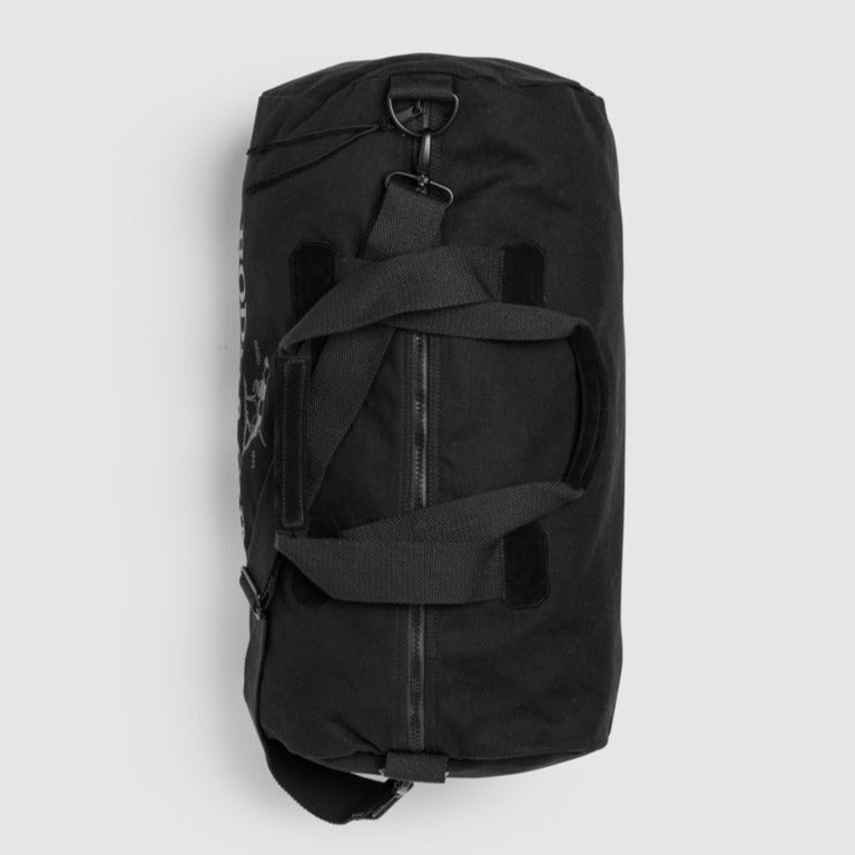 The Rodd & Gunn Richmond Road Duffle Bag, a black cylindrical bag made from durable cotton canvas, is displayed on a light gray background. It includes carrying handles, a top zipper, and an adjustable shoulder strap with metal clasps.