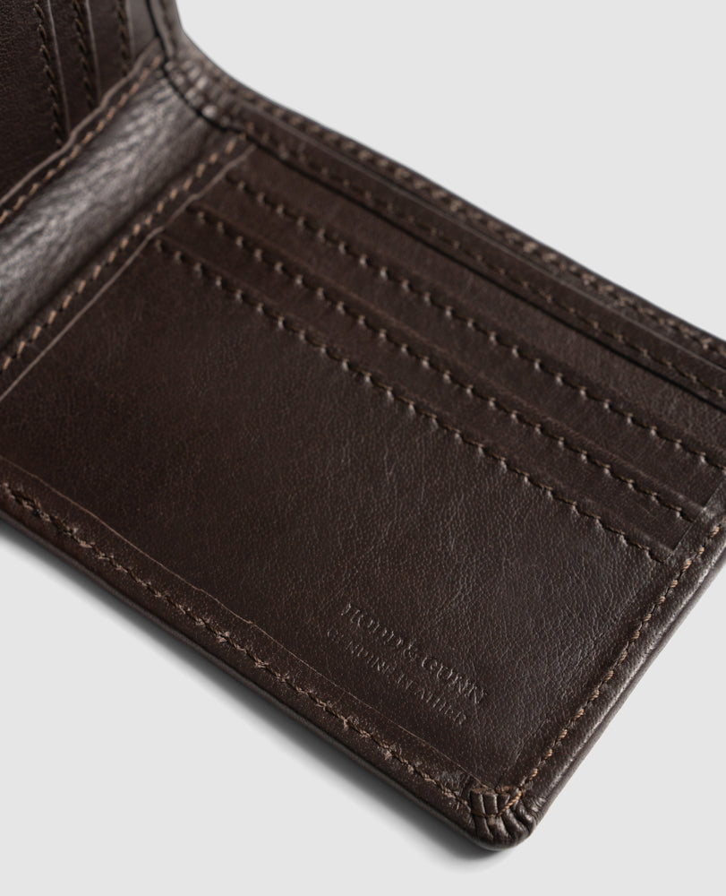 A close-up of an open dark brown leather wallet, the Rodd & Gunn Victoria Flats Road Wallet, crafted from Genuine Buffalo Leather, showing multiple card slots. The interior stitching and leather texture are clearly visible. The bottom right corner is embossed with the text "BEDFORD & SLINK MANHATTAN.