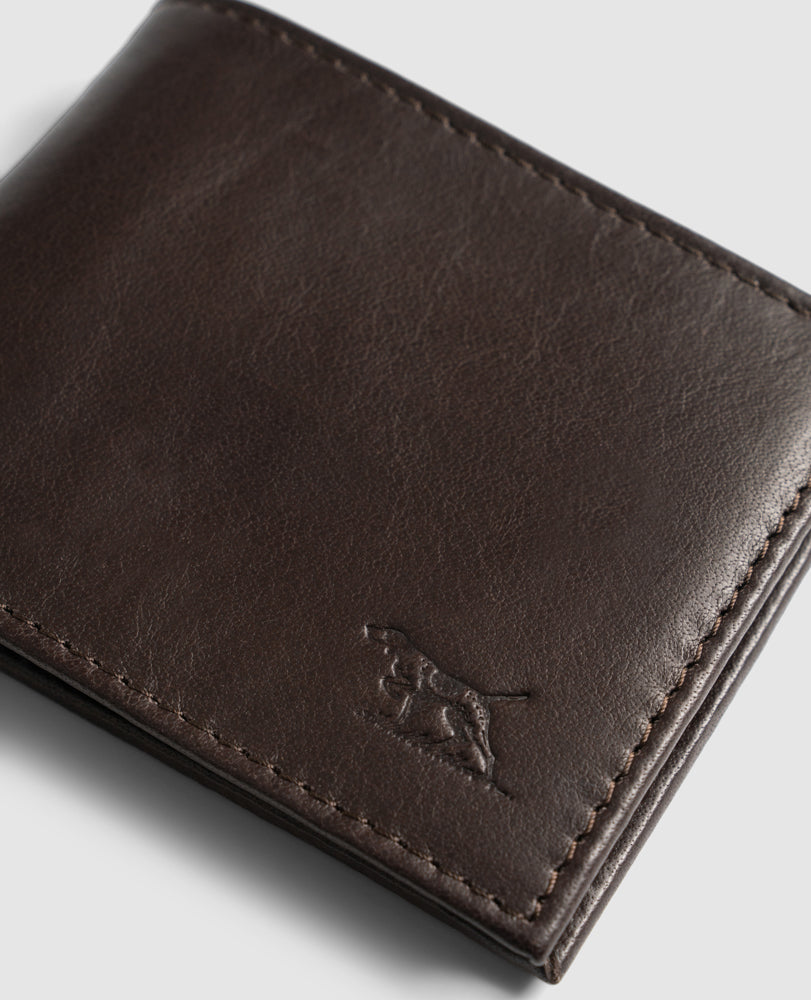 Close-up of a Rodd & Gunn Leeston Dunsandel Road Wallet in dark brown Buffalo Leather with stitched edges and an embossed running dog logo in the lower right corner. It features card slots and a coin pocket against a plain light gray background.