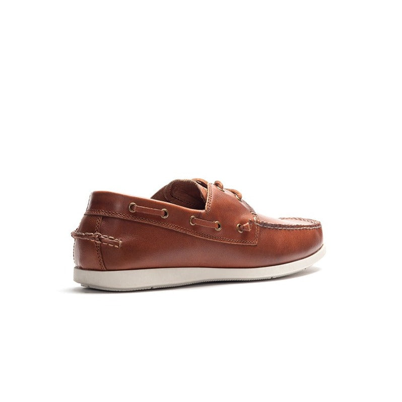 The Rodd & Gunn Gordons Bay Boat Shoe is a brown leather boat shoe featuring a rubber outsole and white stitching, viewed from the side. It boasts a white sole and detailed stitching around the upper edge, along with eyelets threaded with leather laces. The background is white.