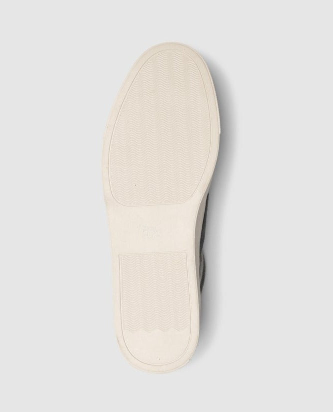 The image displays the sole of the Rodd & Gunn Endeavour Sail Sneaker, boasting a white rubber base with a textured pattern for enhanced grip and a sleek outline. The heel and ball areas have diverse textures to improve traction. Elegance is added with suede leather trims, while the molded footbed ensures supreme comfort. The background is light gray.