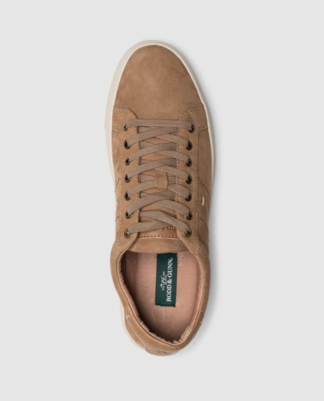 An overhead view of a single tan nubuck leather Rodd & Gunn Endeavour Spirit Sneaker with brown laces on a light gray background highlights its white stitching, classic white rubber sole, and a green insole label with white text.