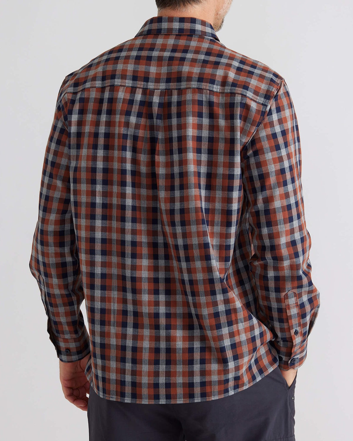 A person models the Breakaway Bilbao Shirt, a long-sleeved, multicolored plaid shirt made of 100% cotton, featuring shades of blue, red, and beige. They stand facing away from the camera and pair it with dark trousers for an elegant look.