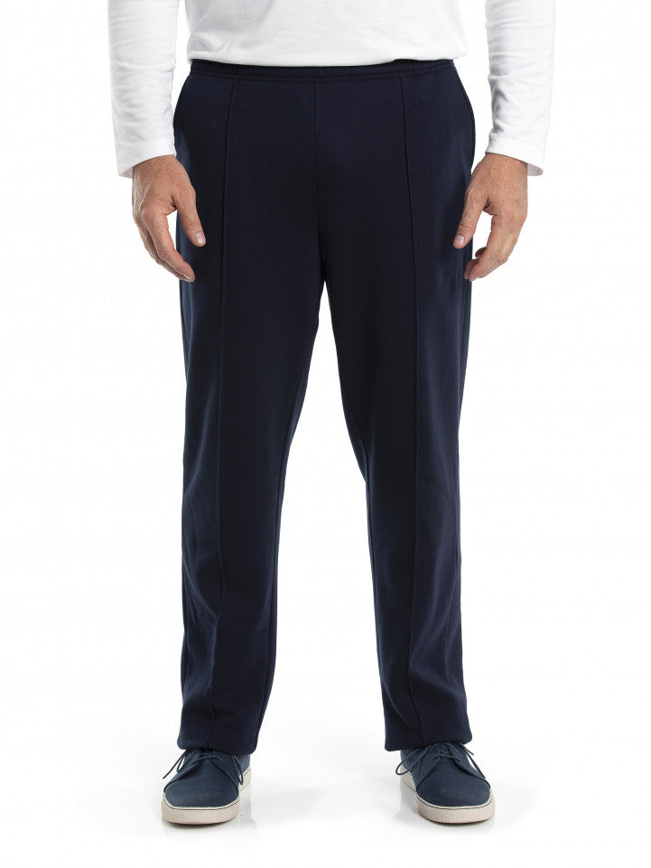 A person in Breakaway Snowy Mt Fleece Pants, dressed in a white long-sleeved shirt, is standing facing forward. Their hands are relaxed by their sides, and they are wearing blue casual shoes with white soles. The background is plain white.