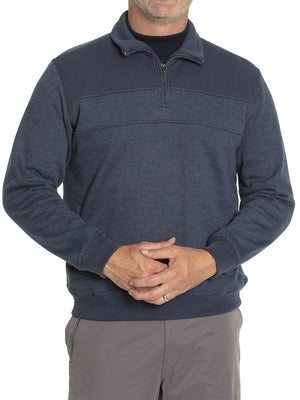 A person wears the Breakaway Zed Snowy Mt Fleece Half Zip in dark blue with a textured shoulder pattern and horizontal chest seam, paired with gray pants, hands clasped. The fleece-lined pullover obscures the person's face.