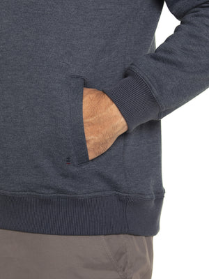 Someone wears the Breakaway Zed Snowy Mt Fleece Half Zip in dark gray as a pullover with ribbed cuffs, their right hand in the pocket. Paired with light gray pants, this cozy fleece-lined outfit contrasts beautifully against the plain white background.