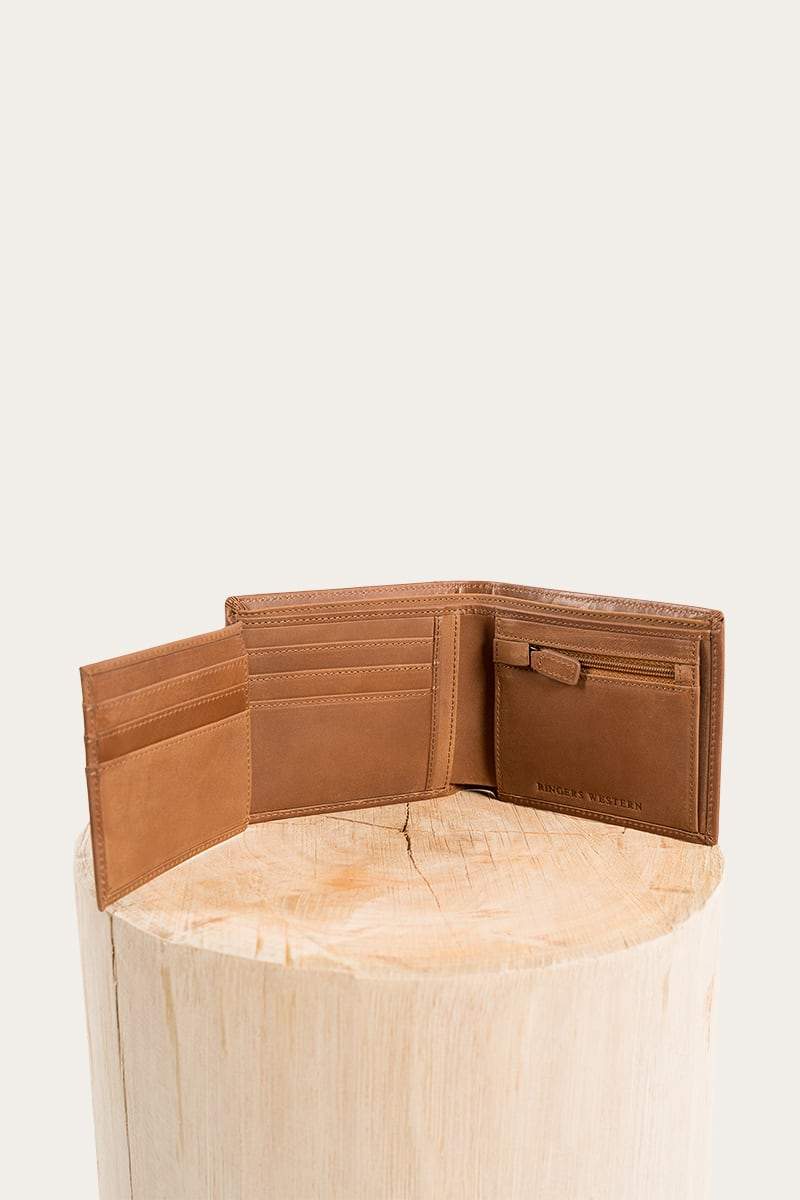 The Ringers Western Bayview Wallet, made from genuine leather, is stylishly open on a wooden pedestal against a plain backdrop. This brown wallet includes multiple card slots and a special compartment for bills.