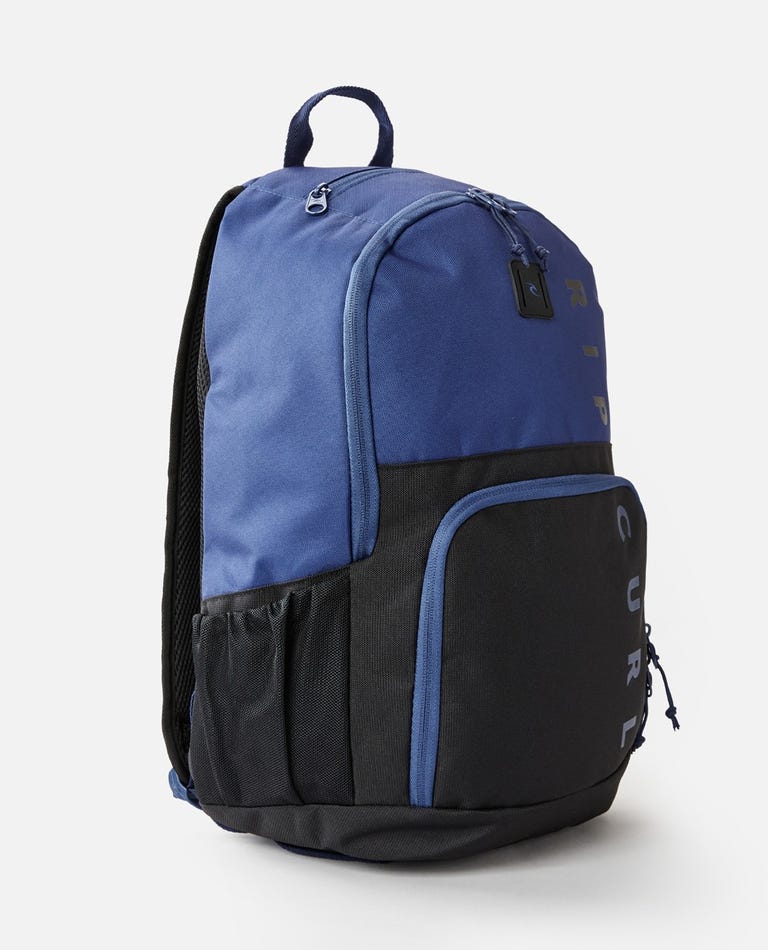 The Rip Curl Evo 24L Hope Eco Backpack in blue and black has a top handle, zipper compartments, a laptop section, side mesh pockets, and "RIP CURL" on the front pocket. Its design is simple and functional.