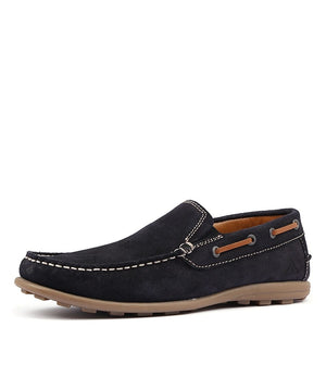 The Colorado Rocana Leather Slip On is a black suede loafer with white stitching, a brown rubber sole, and moccasin-style design. Featuring rawhide lace detailing on the sides, it offers a casual yet sophisticated look in an easy slip-on style.