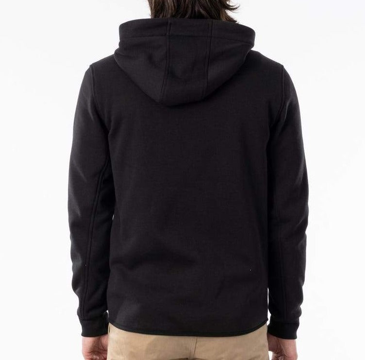 A person with long, dark hair is shown from behind, wearing the Rip Curl Anti Series Departed Zip Thru hoodie in black paired with tan pants. This winter-appropriate hoodie sets a stylish tone against the plain white backdrop.