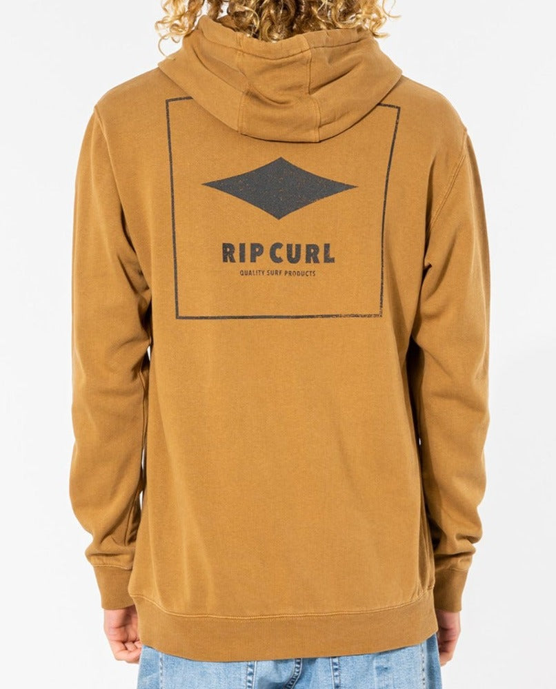 Wearing light blue jeans, a person with curly hair dons the Rip Curl Quality Products Hood, a cozy brown cotton/polyester hoodie featuring "Rip Curl Quality Surf Products" in a bold square design on the back. They stand facing away.