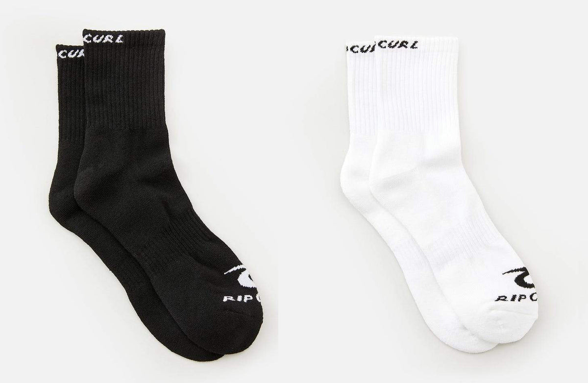 Two pairs of socks from the Rip Curl Corp Crew Sock 5 Pack are displayed side by side. The left pair is black, and the right pair is white. Each sock, designed for men's sizes 9-13, features the brand name written at the top and on the toes in contrasting colors to the sock itself. The background is plain white.