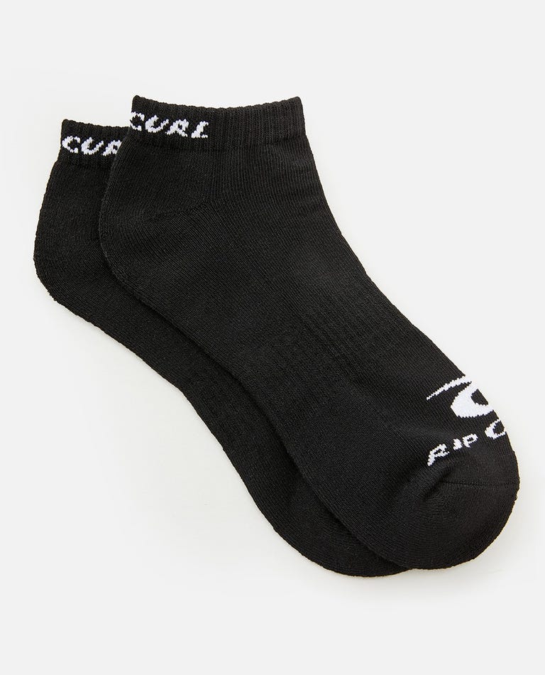 A pair from the Rip Curl Corp Ankle Sock 5 Pack features black ankle socks with a subtle ribbed texture and arch support. These socks showcase white printed text and the Rip Curl logo near the toes, along with the brand name along the top edge. They are displayed overlapping on a white background.