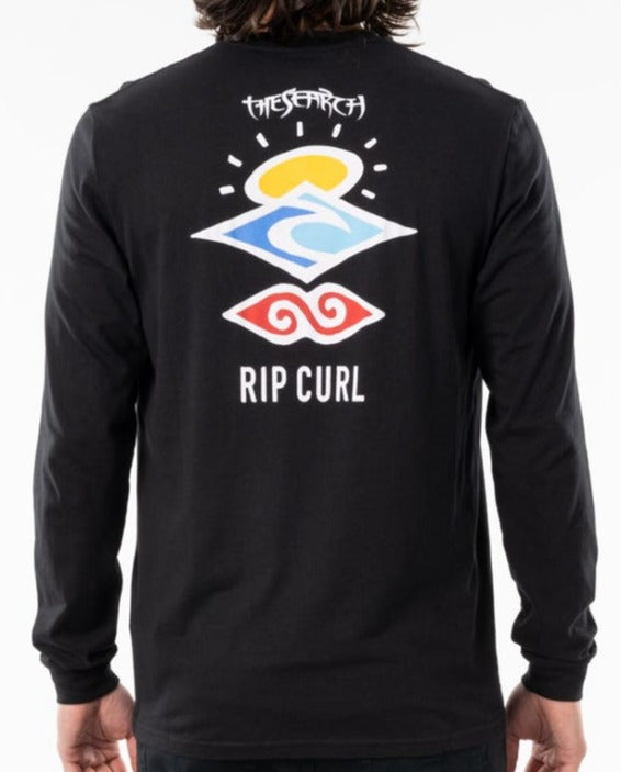 A person wearing a Rip Curl Search Icon Long Sleeve Tee in black. The organic cotton shirt's back features colorful abstract shapes with "THE SEARCH" above and "RIP CURL" below.