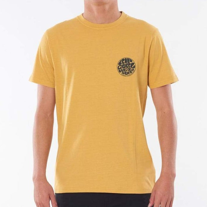 A person wearing the Rip Curl Wetsuit Icon Tee, a plain yellow T-shirt featuring a small circular Rip Curl print logo on the upper left side of the chest. The logo displays stylized text that is somewhat difficult to read. This comfortable tee, made from 100% cotton, sets off against a plain white background.