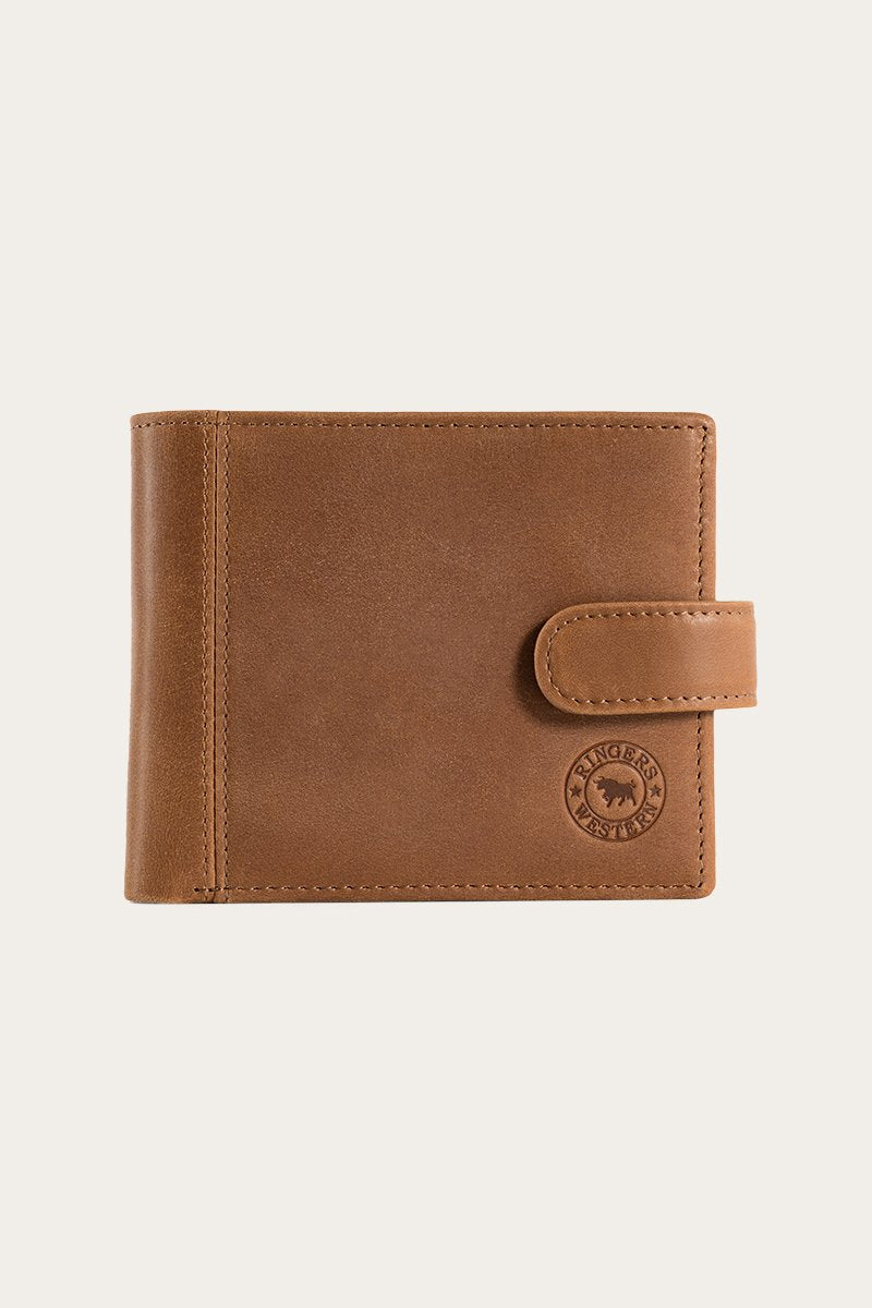 The Ringers Western Cypress Wallet is made from genuine leather with a brown finish and strap closure, showcasing visible stitching and an embossed circular logo on the lower right corner against a plain, light-colored background.