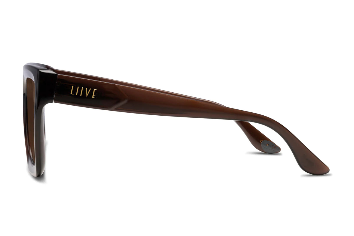 The Liive Desire Xtal Sunglasses feature a side view of brown sunglasses with thick, glossy frames and a gold LIIVE logo on the temple. Made from lightweight polycarbonate for comfort, they also have optically correct lenses for maximum UV protection.