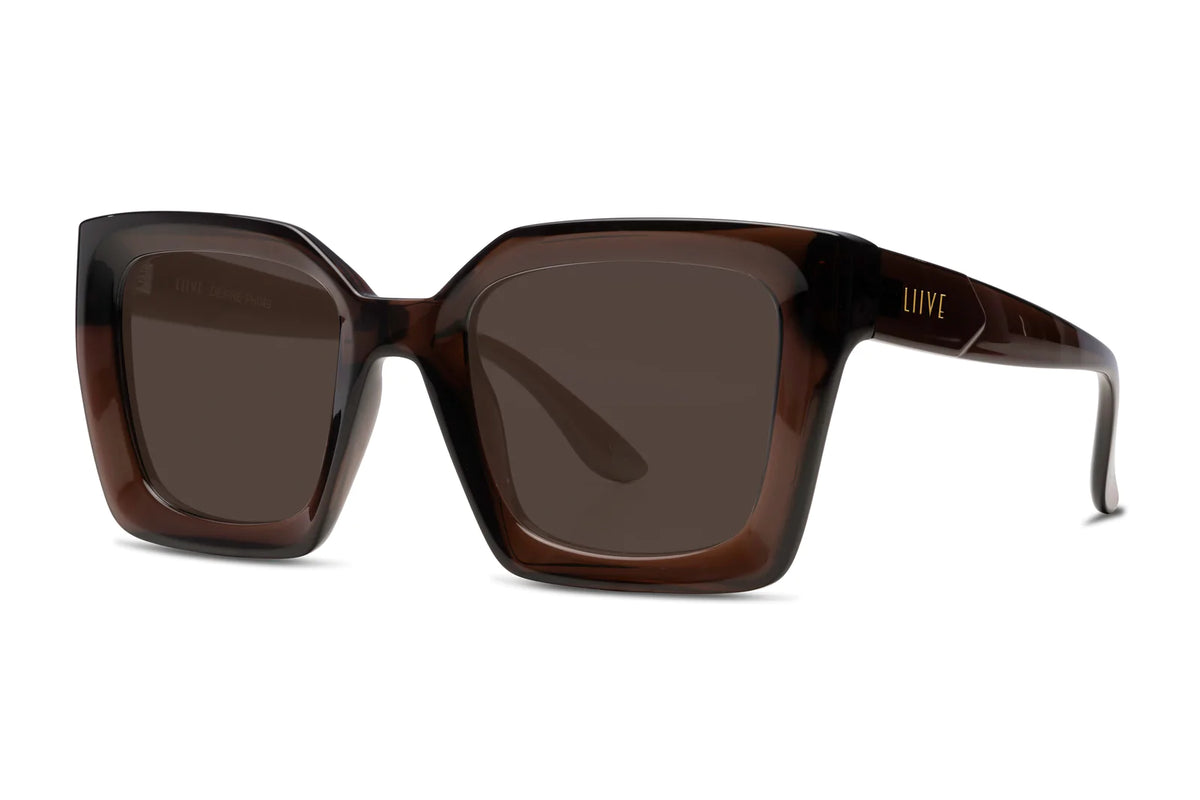 The Liive Desire Xtal Sunglasses feature oversized rectangular frames with dark, optically correct lenses and thick brown frames. "Liive" is elegantly stamped in gold on the temple. With UV protection and a stylish modern design, they're perfect for fashion-conscious wearers.
