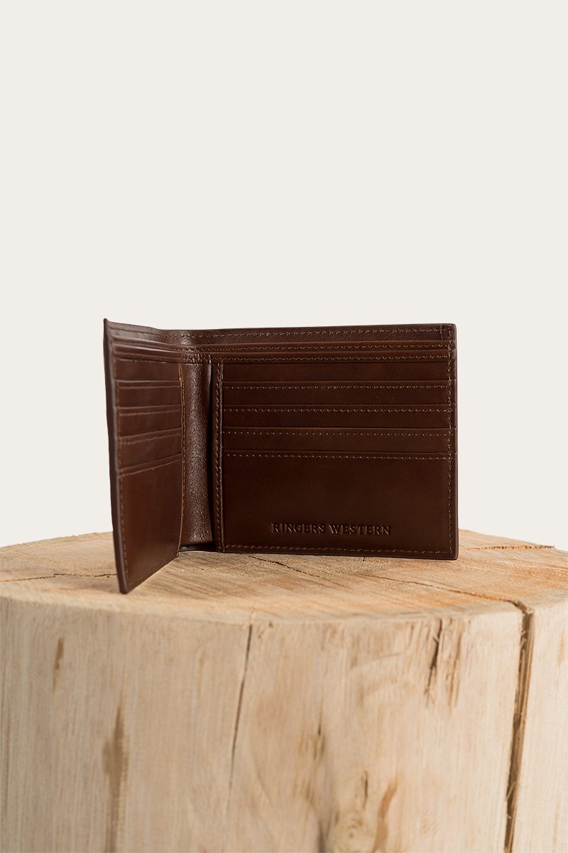 A brown Ringers Western Duke Wallet made of genuine leather with multiple card slots is open and standing upright on a wooden block. The text "KINGSLEY WESTERN" is embossed on the lower right corner of the wallet. The background is plain and light-colored.