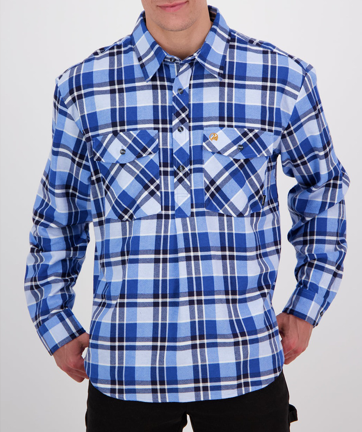 A person wearing a shirt from the Swanndri Egmont Flannelette Twin Pack, featuring a blue, white, and black plaid pattern with two chest pockets and dark pants, stands against a plain white background. The brushed cotton shirt has a small logo on one of the pockets, and the person's hands are placed in their pants pockets.
