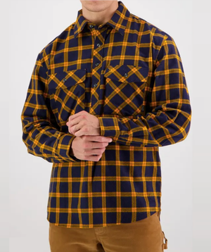 A person is wearing the Swanndri Egmont Flannelette Twin Pack, featuring a soft brushed cotton button-up with a yellow and navy plaid pattern and two chest pockets. They pair it with brown pants against a plain white backdrop.