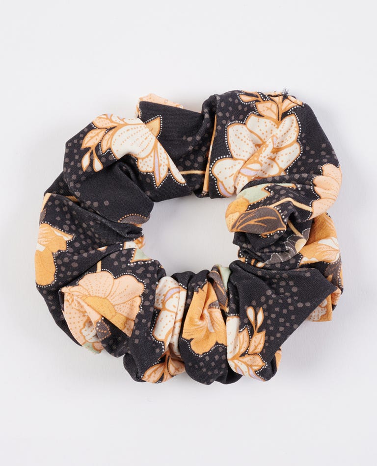 Meet the Rip Curl Gypsy Scrunchie, a stylish microfibre accessory adorned with orange and cream floral patterns on a classic black backdrop, beautifully gathered into an elegant circular design.