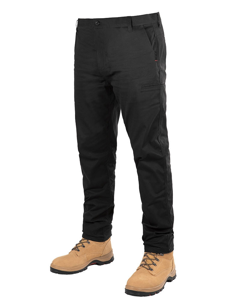 A person wearing UNIT Ignition Stretch Pants in durable black stands against a white background. The pants, featuring side and front pockets, are crafted from stretch fabric for added flexibility. The person is also wearing tan work boots with brown laces. The upper body is not visible.