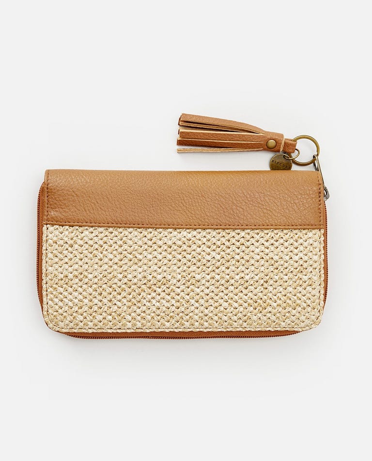 The Rip Curl Surf Gypsy Oversized wallet features a smooth tan leather top and a beige woven bottom. It has a zipper closure with an attached removable tassel keyring and a small round charm. The background is white.