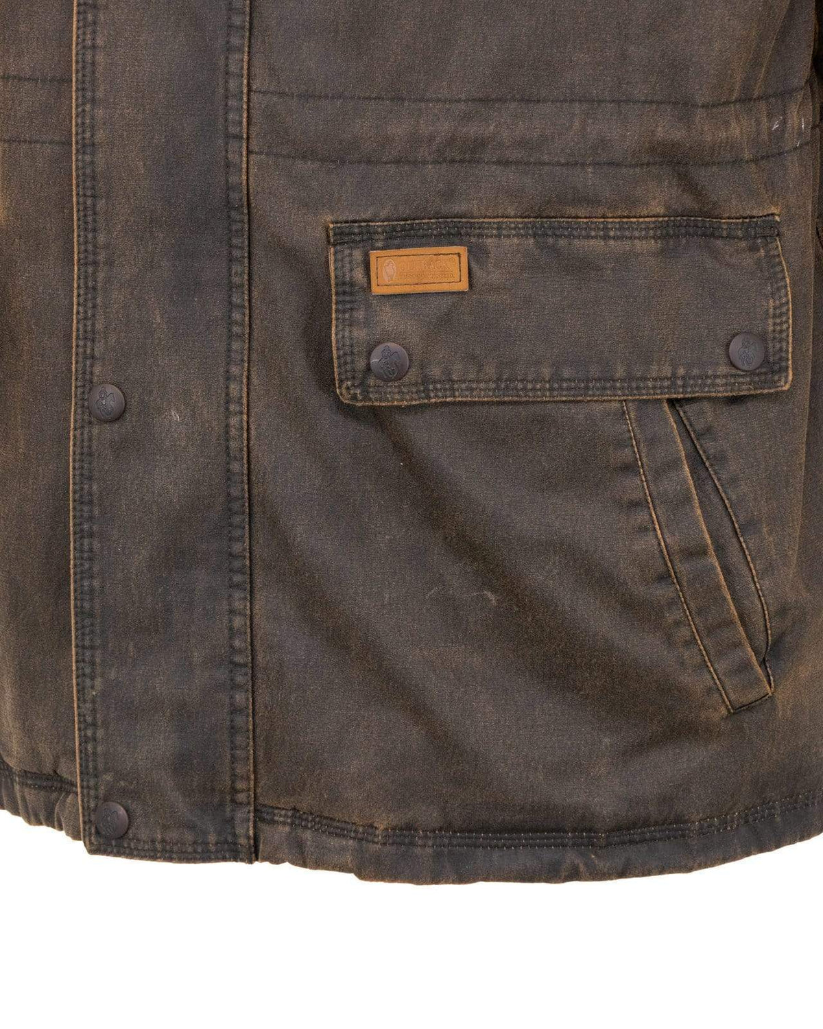 A close-up view of the Outback Ranchers Jacket showcases its weathered brown, hard-wearing fabric with buttoned pockets on the right side and visible stitching details. The material shows signs of wear, and there is a small rectangular leather patch sewn above the pocket, hinting at its previous adventures.