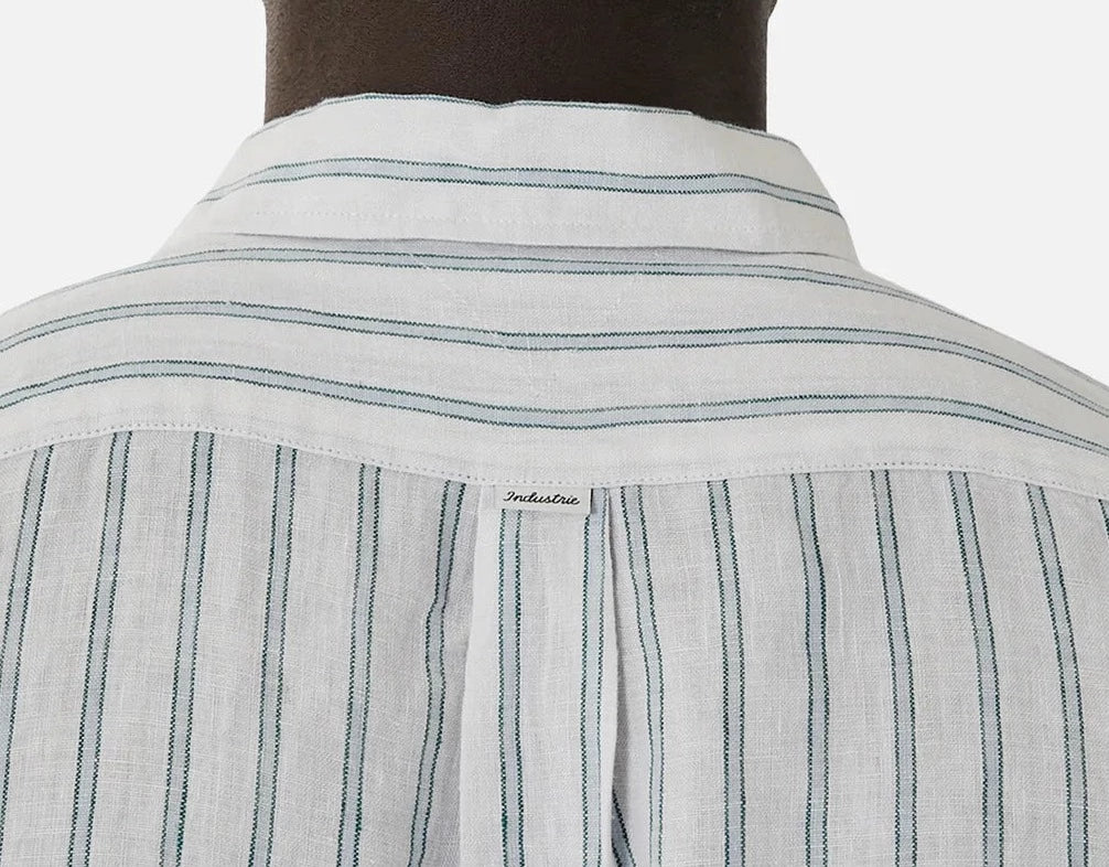 A person is seen from behind wearing the Industrie The Paglia Long Sleeve Shirt, a relaxed fit made of 100% linen. It features thin vertical green stripes, a straight collar, back yoke, and an embroidered tag in the center against a plain white background.