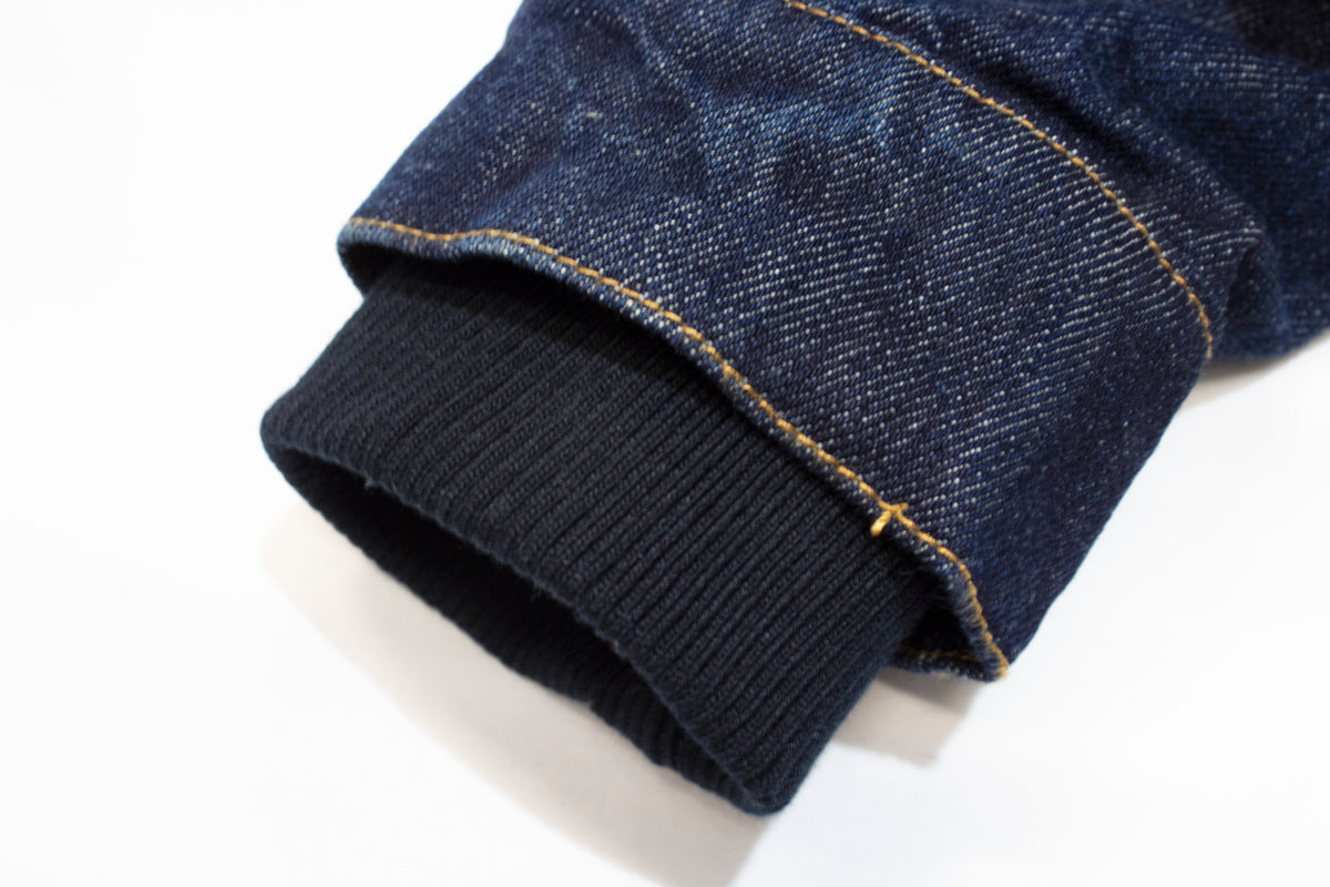 Close-up of the Pilbara Ladies Denim Jacket's cuff, showcasing yellow stitching and ribbed black fabric lining, crafted from 100% cotton against a white background.