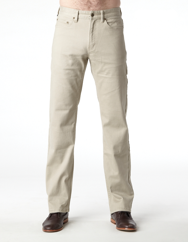 A person stands against a plain white background, wearing the chic Riders Straight Pant Stretch in beige and polished brown leather shoes. The person's hands and upper body are not visible in the image. The straight-legged pants offer a sophisticated look, while the shoes have a refined appearance.