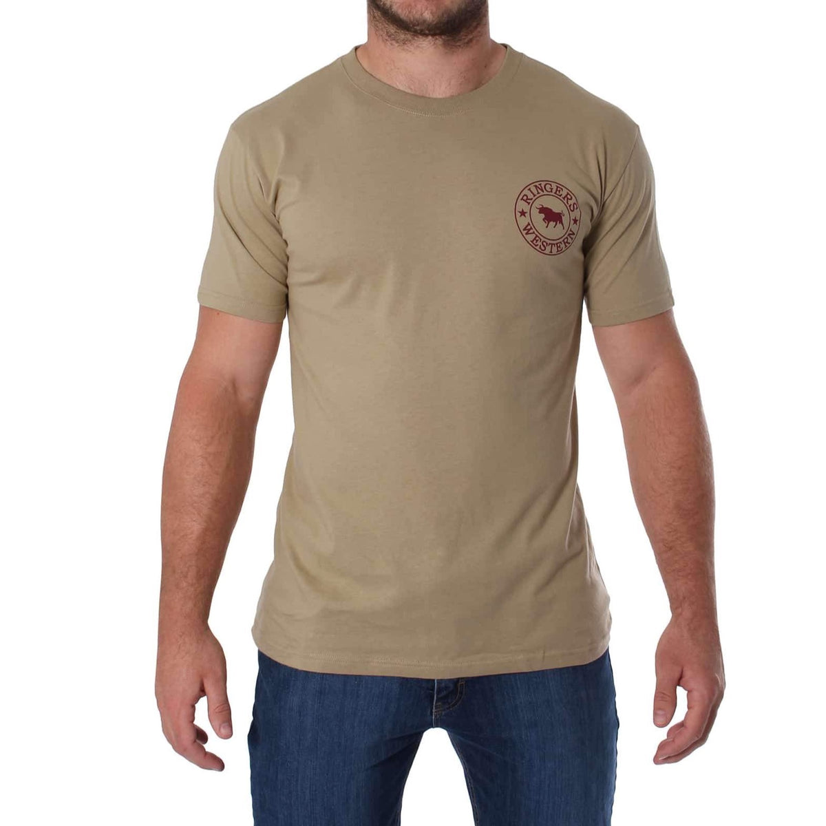 A person wearing a comfortable, plain beige Ringers Western Signature Bull Classic T-Shirt with a small maroon circular logo on the left side of the chest and blue jeans is standing with arms relaxed by their sides. The background is plain white.