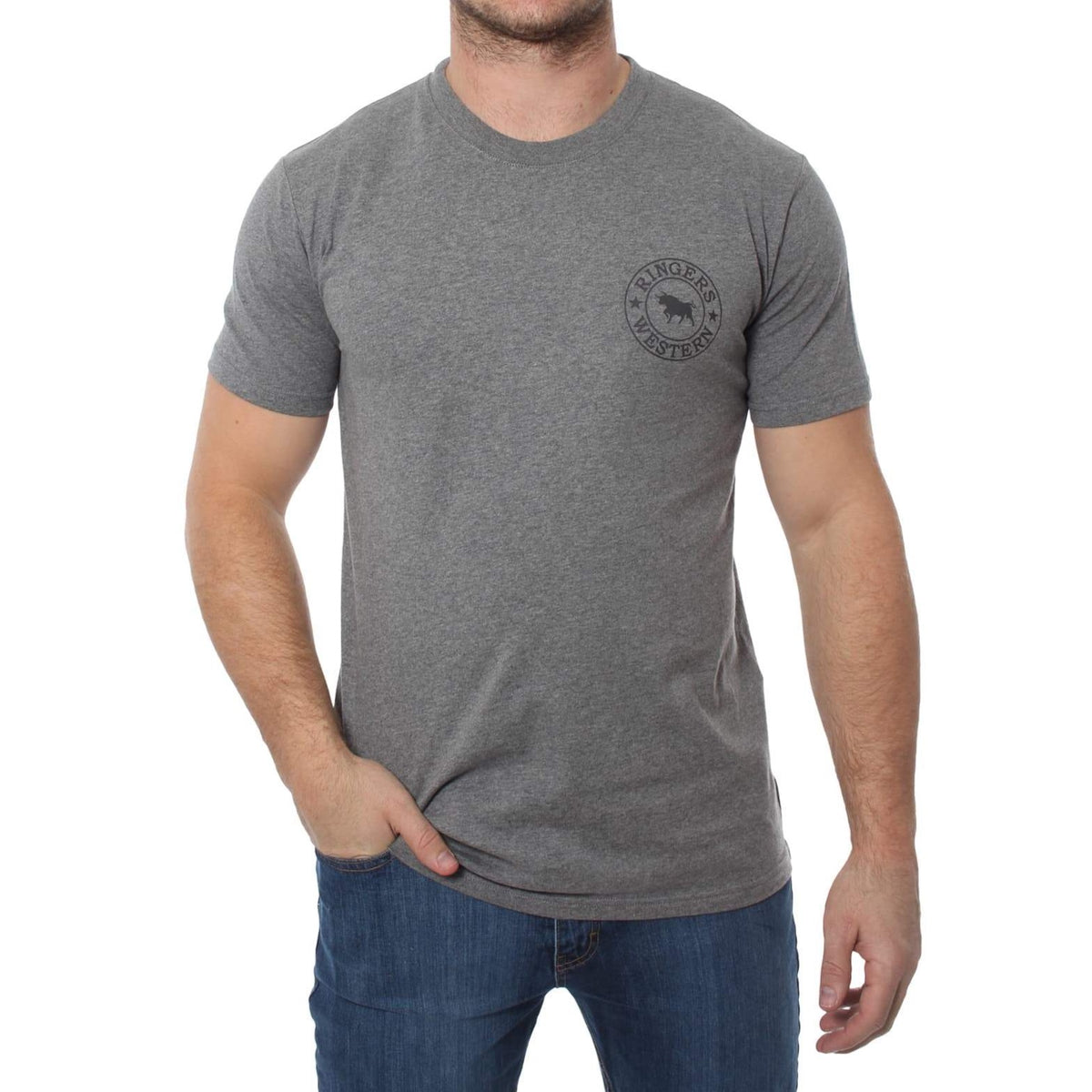 A person is standing with one hand in a pocket, wearing the Ringers Western Signature Bull Classic T-Shirt in plain grey, featuring a small round emblem with text and a graphic on the left chest area, paired with blue jeans. The face is not visible.