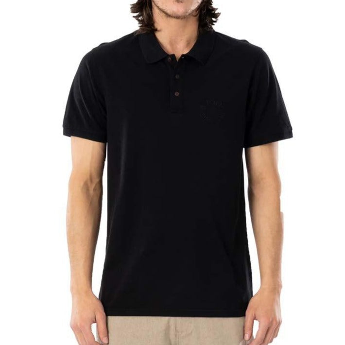 A man stands against a white background wearing a black Rip Curl Faded Polo and beige pants. The image is cropped from the shoulders down, giving off a casual vibe.