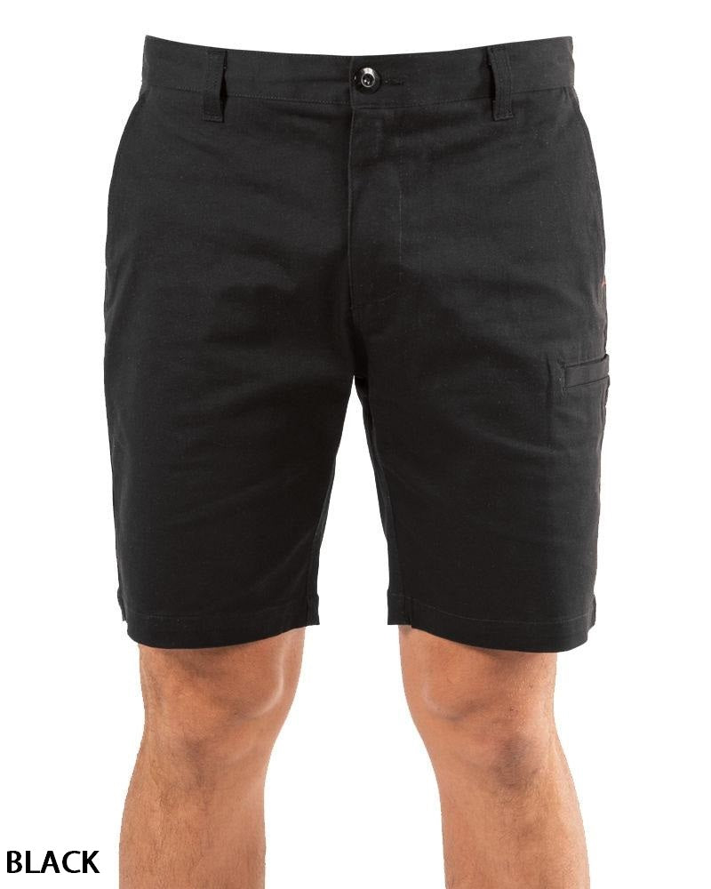 A person wears UNIT Ignition Stretch Short in black—durable stretch fabric, knee-length, with button and zipper closure, front and side pockets. Only the lower torso and upper legs are visible. “BLACK” appears in the bottom left corner.