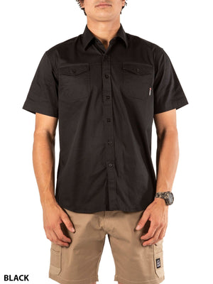A person wears the UNIT Craftman Stretch Short Sleeve Shirt in black with two chest pockets and tan cargo shorts. The stretch-fit shirt offers comfort as they stand facing forward, hands by their sides.