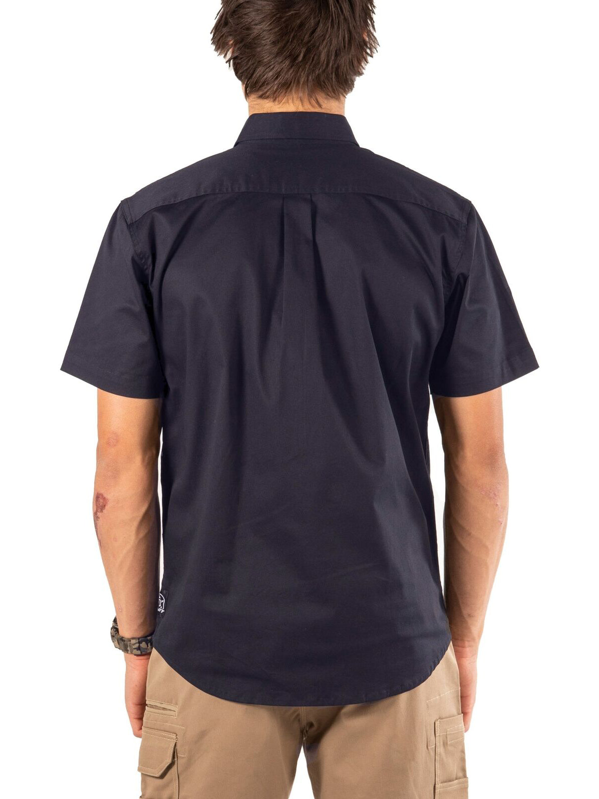 A man wearing the UNIT Craftman Stretch Short Sleeve Shirt in navy and khaki pants stands facing away from the camera against a white background.