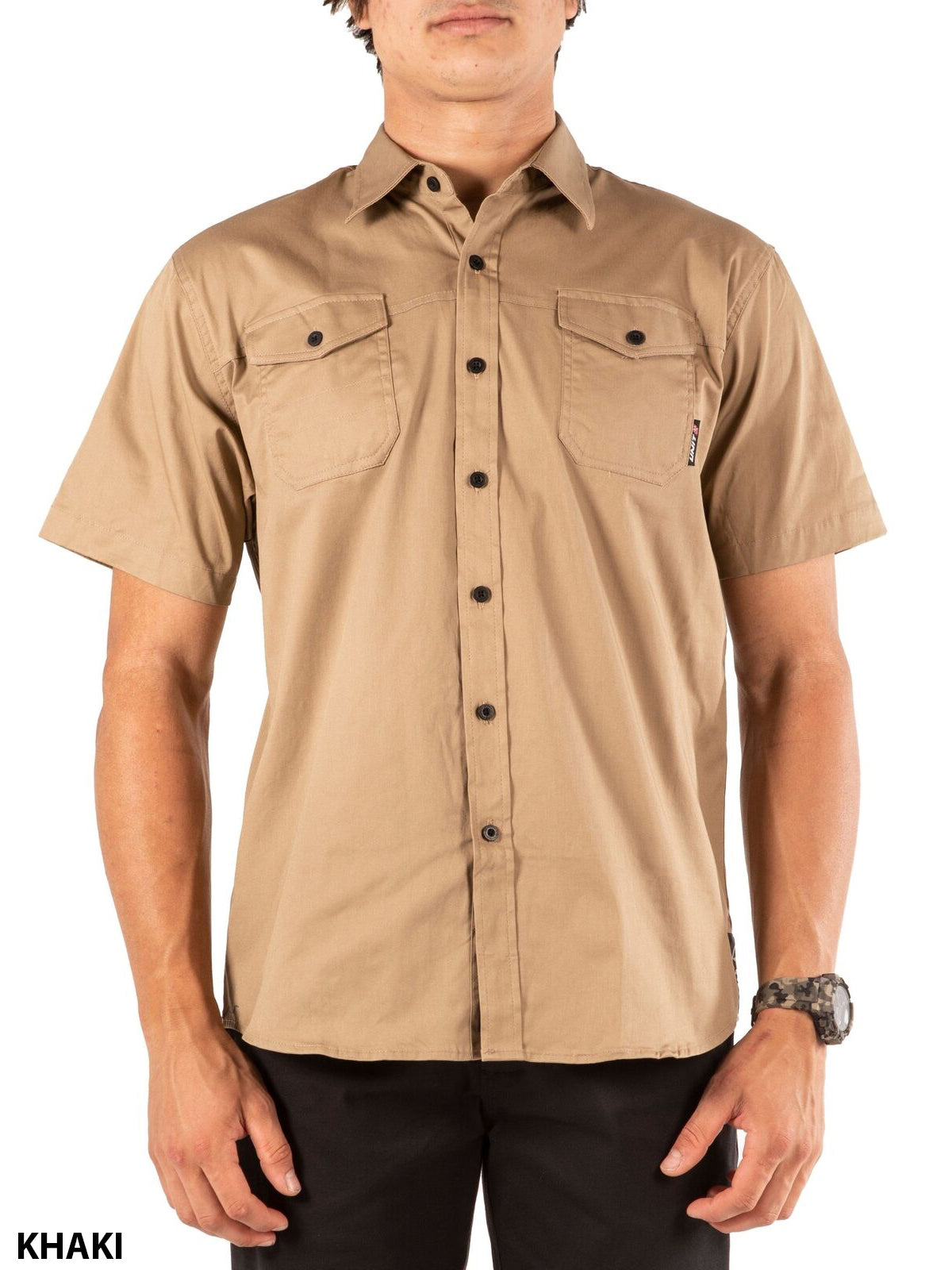 A person wearing the UNIT Craftman Stretch Short Sleeve Shirt in khaki, featuring two chest pockets and black buttons, stands against a white background. The word "KHAKI" is displayed in the bottom left corner.