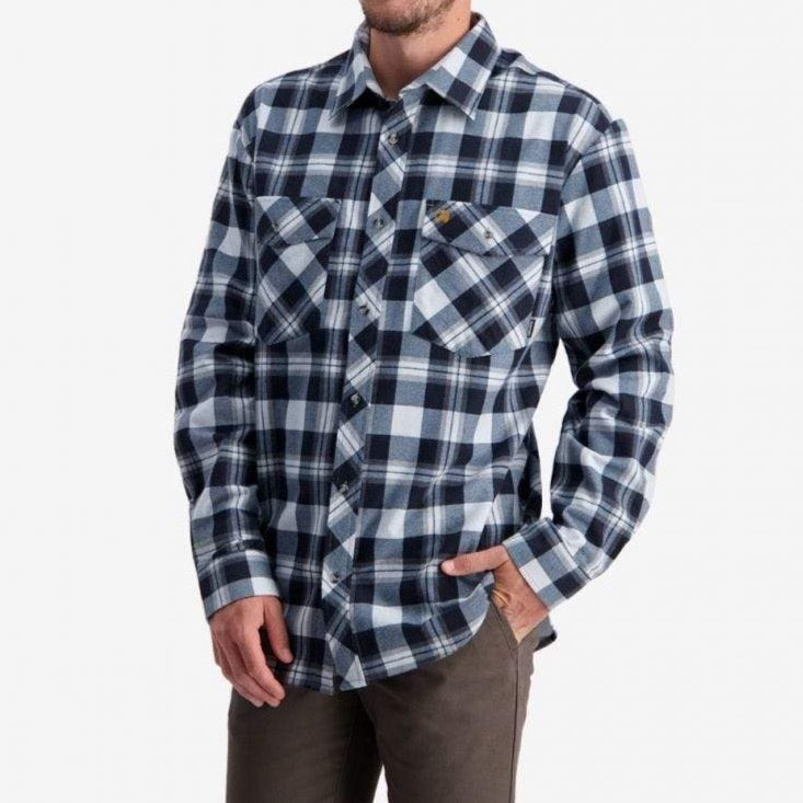 A man wearing a Swanndri Egmont Full Button Flannelette shirt from the Twin Pack, featuring 100% brushed cotton in a blue and white checkered pattern, long sleeves, and two chest pockets, is buttoned up and partially tucked into brown pants. He stands against a plain white background with his face not visible.