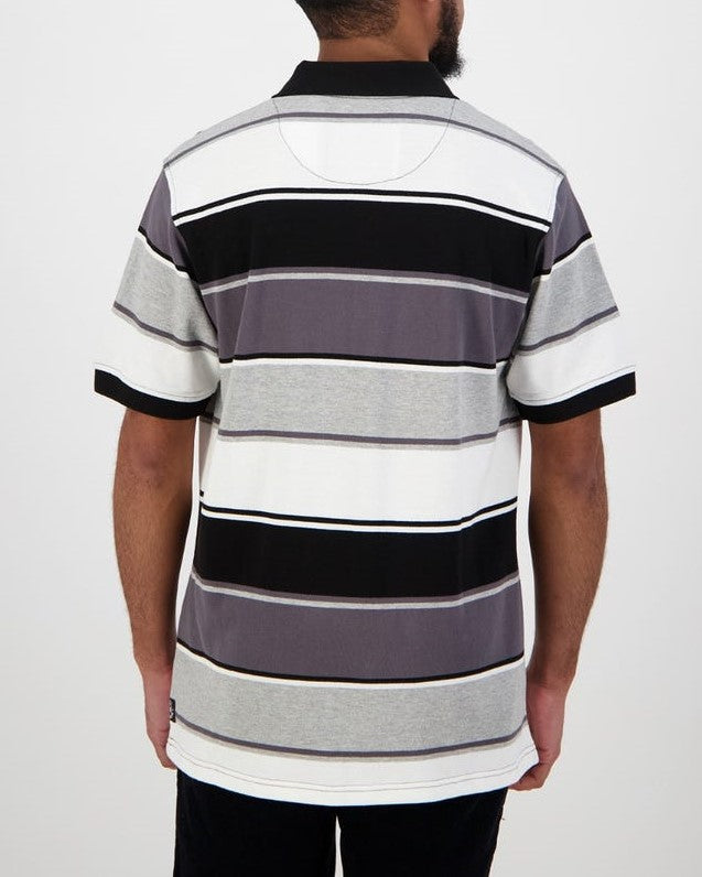 A man with short hair and a beard faces away from the camera, dressed in a Swanndri Kingfield Stripe Polo. This 100% cotton shirt boasts black, gray, and white horizontal stripes with a classic black collar, exuding casual elegance.