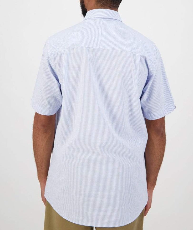 A person in a Swanndri Hinsdale Shirt, light blue and white striped, stands against a white background. This short-sleeve shirt has a classic fit with a classic collar and straight hemline, crafted from 100% cotton for ultimate comfort. They're wearing it with khaki pants.