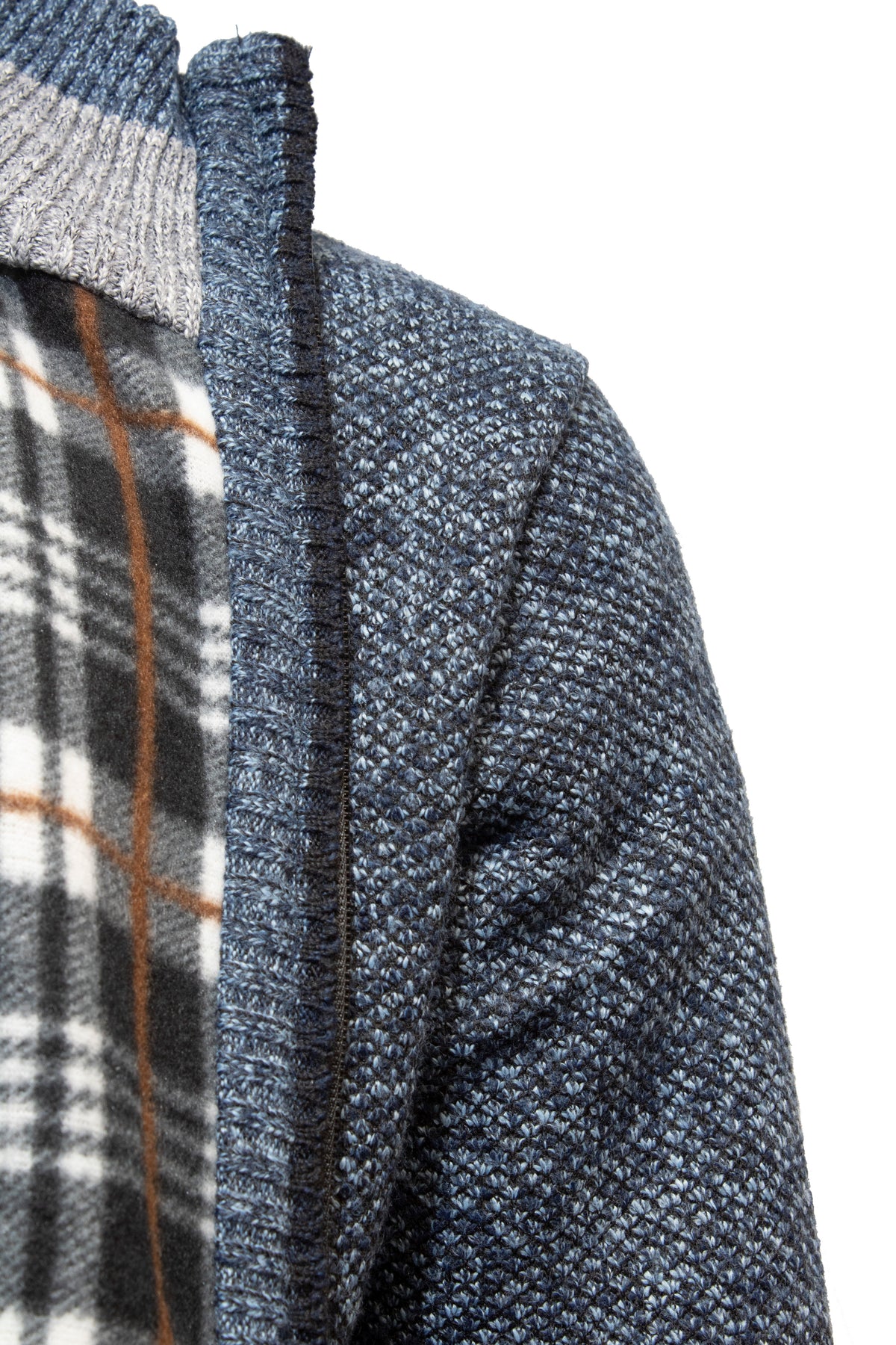 Close-up of a shoulder in a textured knit Sugar Kendry Full Zip Polar Fleece Cardigan, dark blue with ribbed details, over a gray and white plaid shirt with brown stripes. The zipper adds functionality to this stylish ensemble, ideal for layering on cooler days.