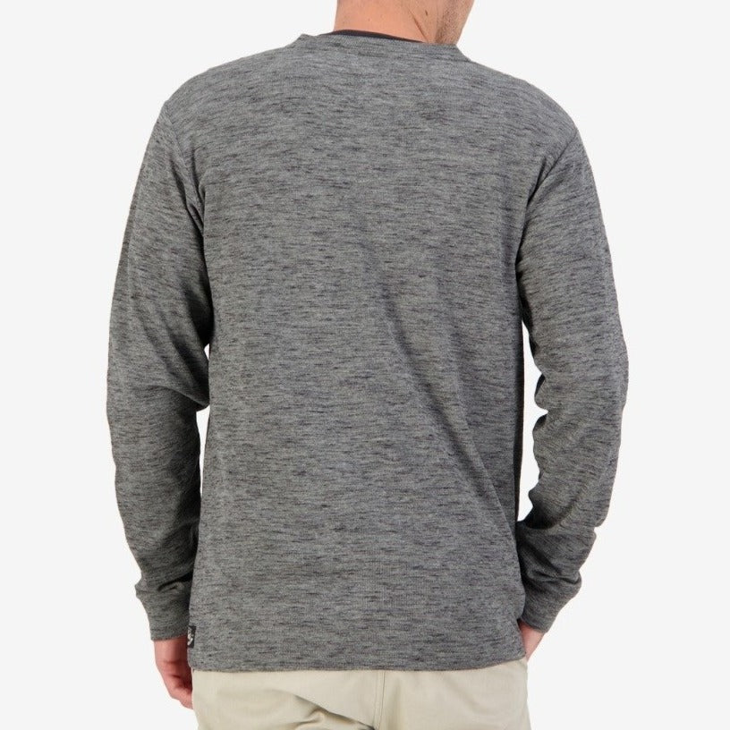 A person stands facing away, wearing the Swanndri Oxford Henley in heather gray with waffle knit detailing and light beige pants. The 100% cotton fabric ensures comfort against the plain white background, highlighting their upper body and the back of their clothing.